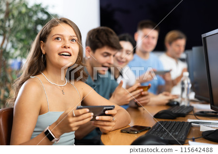 At computer class, young girl student sits with mobile phone and listens admiringly to teacher At computer class, young girl student sits with mobile phone and listens admiringly to teacher 115642488