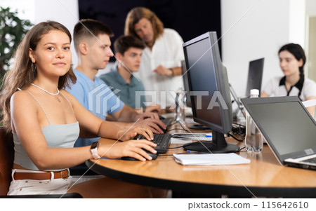 Enthusiastic young girl studying in computer lab with fellow students 115642610