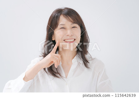Middle-aged woman pointing at her mouth 115642639