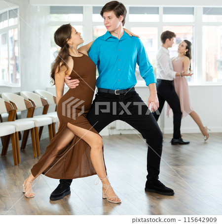 Couple in evening dresses enjoys pair dance tango, interacting with each other on floor 115642909