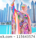 Beautiful Stylish Young Muslim Woman in Colorful Hijab and Rainbow Sunglasses Raised Her Hand, Skyscrapers and Blue Water, Ocean on Background. AI Generated Vertical. Fashion and Vacation 115643574