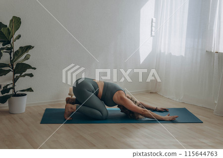A 50-year-old woman does yoga at home 115644763