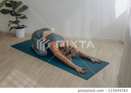 A 50-year-old woman does yoga at home 115644765