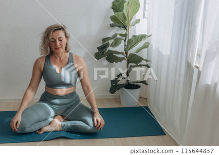 A 50-year-old woman does yoga at home 115644837