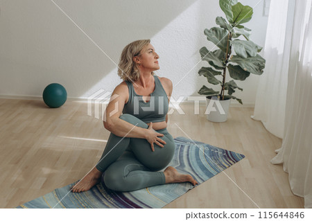 A 50-year-old woman does yoga at home 115644846