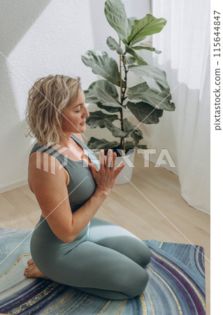 A 50-year-old woman does yoga at home 115644847
