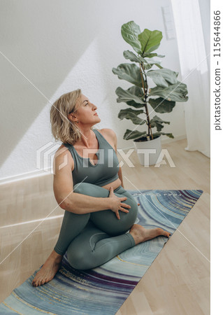 A 50-year-old woman does yoga at home 115644866