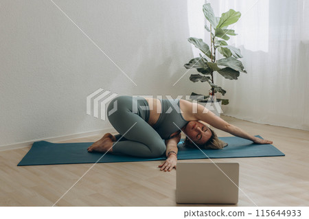 A 50-year-old woman does yoga at home 115644933