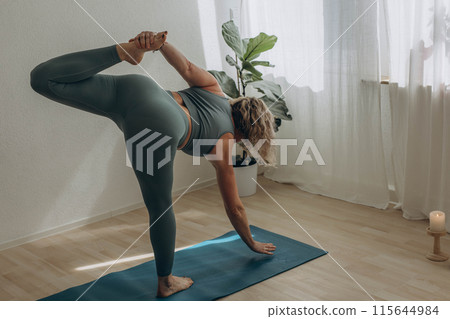 A 50-year-old woman does yoga at home 115644984