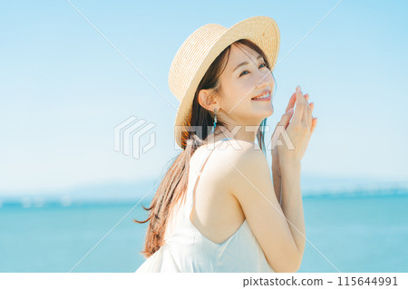 A woman wearing a straw hat with the sea and blue sky in the background A woman wearing a straw hat with the sea and blue sky in the background 115644991