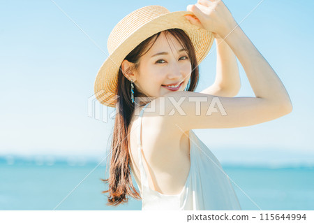 A woman wearing a straw hat with the sea and blue sky in the background 115644994