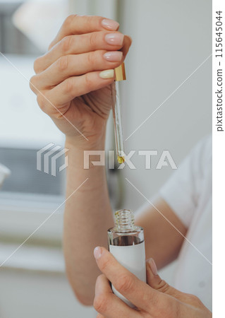 A woman's hand delicately holds a bottle with a dropper, showcasing elegance and precision A woman's hand delicately holds a bottle with a dropper, showcasing elegance and precision 115645044