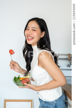 An attractive, smiling young Asian woman holding a healthy salad bowl, standing in the kitchen. An attractive, smiling young Asian woman holding a healthy salad bowl, standing in the kitchen. 115645045