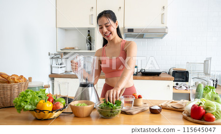 A beautiful, healthy Asian woman in sportswear is making her healthy smoothie drink in the kitchen. A beautiful, healthy Asian woman in sportswear is making her healthy smoothie drink in the kitchen. 115645047