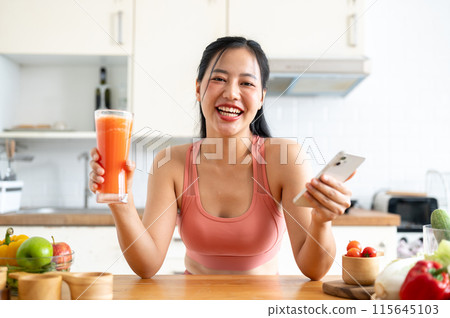 A healthy Asian woman in sportswear holding her phone and a glass of fresh smoothie juice. A healthy Asian woman in sportswear holding her phone and a glass of fresh smoothie juice. 115645103