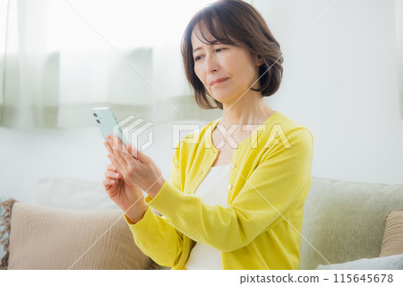 A middle woman who operates a smartphone in the living room A middle woman who operates a smartphone in the living room 115645678