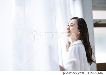 一個打開窗簾的年輕女子 115646687