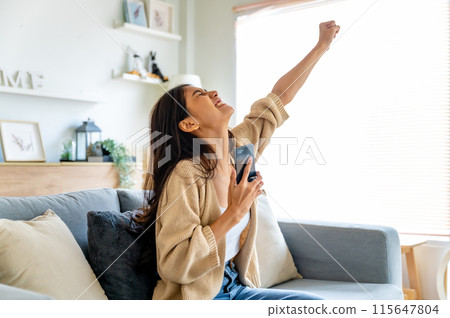 Happy young asian woman relax on comfortable couch at home texting messaging on smartphone 115647804