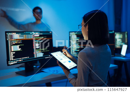 UX designer works on a tablet while a colleague tests  application in the background in office 115647927