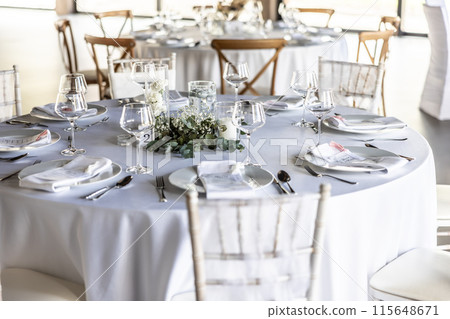 A wedding table covered with a white tablecloth, decorated with flowers, candles, glasses and cutlery. A wedding table covered with a white tablecloth, decorated with flowers, candles, glasses and cutlery. 115648671