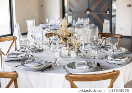 A wedding table covered with a white tablecloth, decorated with flowers, candles, glasses and cutlery. A wedding table covered with a white tablecloth, decorated with flowers, candles, glasses and cutlery. 115648676