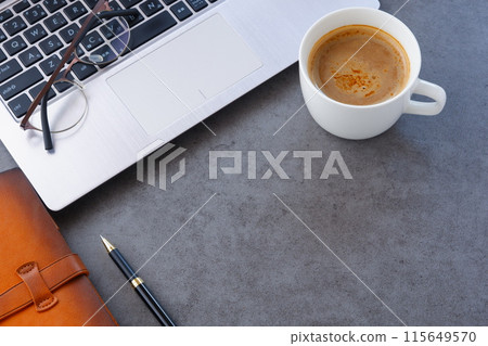 An image of someone working at a desk with a laptop and a personal organizer while drinking freshly brewed coffee 115649570