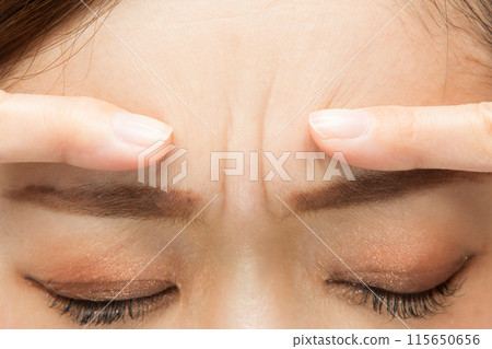 The woman points to the wrinkles between her eyebrows. 115650656