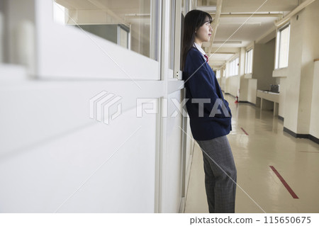 Female high school student wearing slacks leaning against the wall in the hallway Diversity 115650675