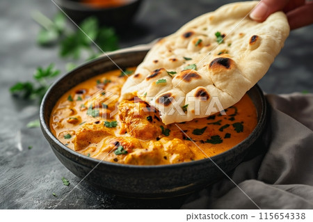 Bowl of rich curry paired with naan bread, sprinkled with herbs for an authentic meal 115654338