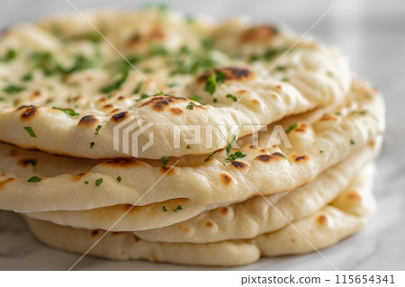 Stack of soft naan bread, lightly seasoned and ready to accompany any meal 115654341