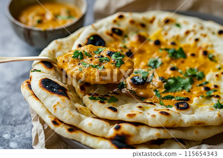 Hand scooping creamy curry with naan bread, highlighting traditional Indian flavors 115654343
