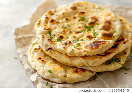 Stack of warm naan bread garnished with fresh herbs, wrapped in paper 115654349