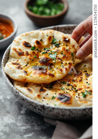 Freshly baked naan bread garnished with herbs, being lifted from a rustic bow Freshly baked naan bread garnished with herbs, being lifted from a rustic bow 115654350