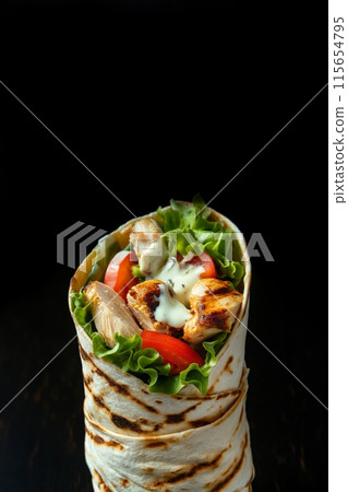 Succulent chicken and fresh vegetable wrap highlighted by a dark, elegant background Succulent chicken and fresh vegetable wrap highlighted by a dark, elegant background 115654795