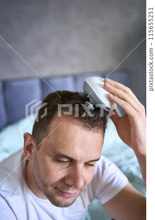 a man massages his head with an electric massager for hair growth a man massages his head with an electric massager for hair growth 115655251