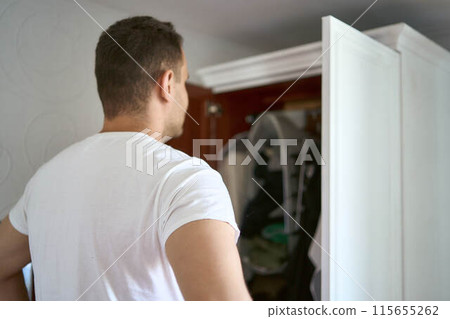 the man looks in the wardrobe and chooses what to wear 115655262