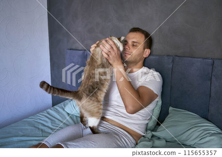 a  young man pet a cat in bed, morning routine 115655357