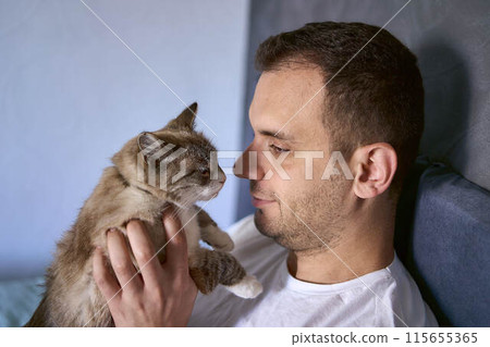 a  young man pet a cat in bed, morning routine 115655365