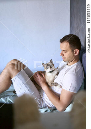 a young man pet a cat in bed, morning routine a young man pet a cat in bed, morning routine 115655369