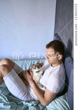 a  young man pet a cat in bed, morning routine 115655372