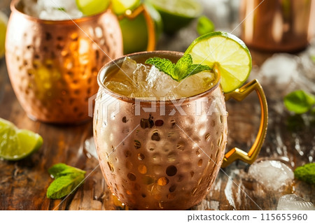 Chilled cocktail in a textured copper mug garnished with lime and mint, on a wooden surface 115655960