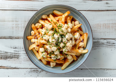 Delightful poutine with crispy fries and cheese curds in a gray bowl on a rustic table 115656024
