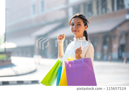 Young Woman Smiling While Holding Shopping Bags Outdoors 115657529