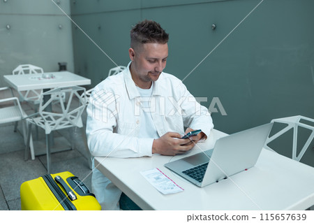 Young Caucasian male passenger in stylish casual clothes using smartphone and laptop keyboard, sit has training online meeting on laptop computer in airline lounge wait transit international airport Young Caucasian male passenger in stylish casual clothes using smartphone and laptop keyboard, sit has training online meeting on laptop computer in airline lounge wait transit international airport 115657639