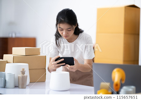 Young Asian business entrepreneur using a smartphone take a photo of product for upload to website online shop. 115657651