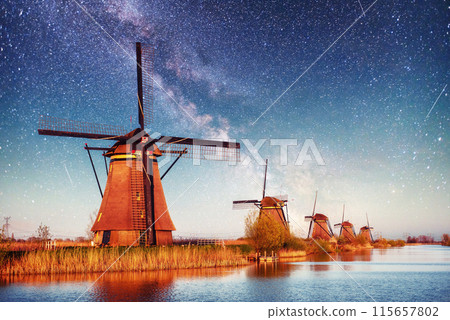 Colorful spring night with traditional Dutch windmills canal in Rotterdam. Wooden pier near the lake shore. Holland. Netherlands. Fantastic starry sky and the milky way Colorful spring night with traditional Dutch windmills canal in Rotterdam. Wooden pier near the lake shore. Holland. Netherlands. Fantastic starry sky and the milky way 115657802