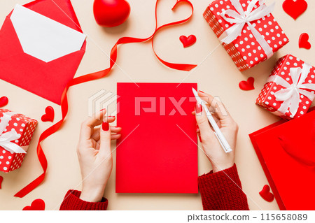 top view photo of valentine day decor female hands holding letter with envelope, small gift box and heart decoration on isolated pastel colored background with empty space top view photo of valentine day decor female hands holding letter with envelope, small gift box and heart decoration on isolated pastel colored background with empty space 115658089