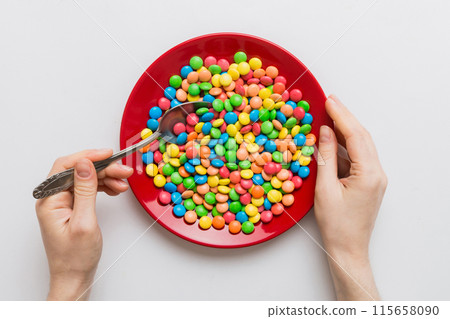 the girl holds cutlery in her hands and eats sweets in a plate. Health and obesity concept, top view on colored background 115658090