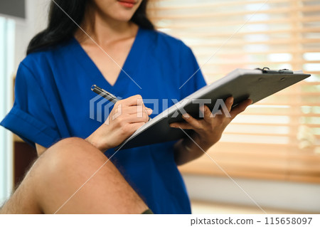 Closeup physiotherapist examining patient with knee injury and recording condition on clipboard 115658097