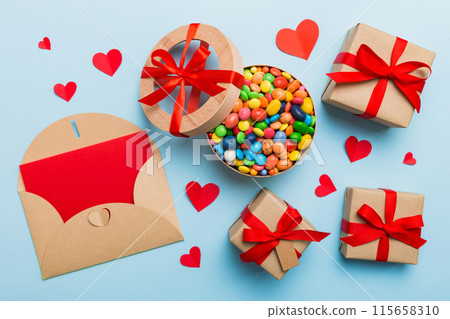 Red envelope with candy and gift box and Valentines hearts on colored background. Flat lay, top view. Romantic love letter for Holiday concept Red envelope with candy and gift box and Valentines hearts on colored background. Flat lay, top view. Romantic love letter for Holiday concept 115658310
